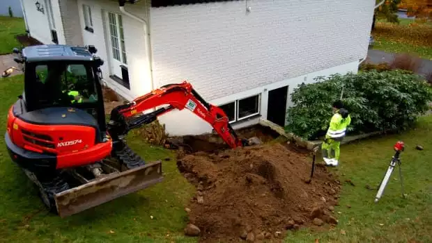 Minigrävare gräver för ny dränering längs en villa
